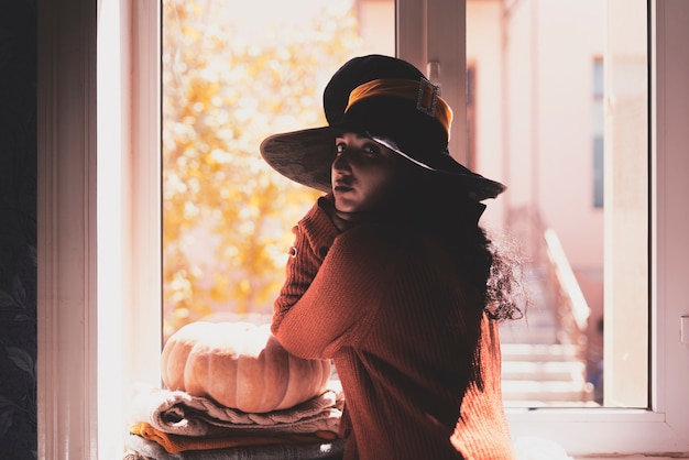 Halloween lady wearing witch cup a woman in witch hat and halloween pumpkin near the windows portrai...