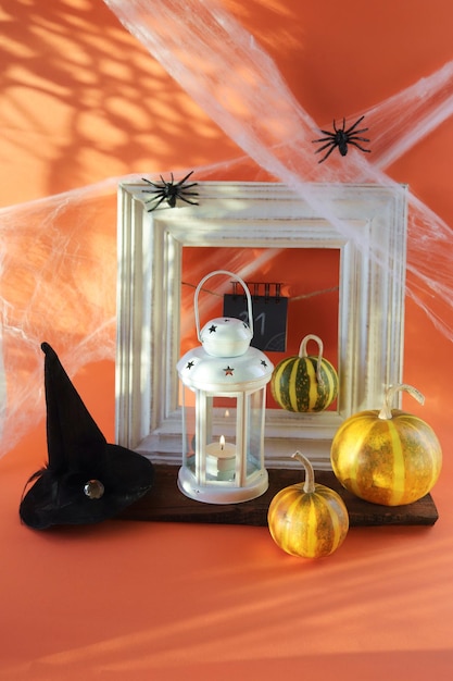 Halloween, a lantern with a burning candle, pumpkins, a witch's hat, cobwebs with spiders