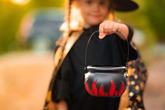 Halloween Little girl in witch hat with candy bucket Toddler in witch costume playing in autumn park