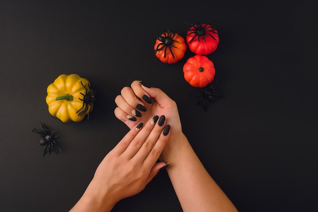 Halloween Nail Art Design. Flat lay with pumpkins, spiders and beautiful manicure on hands on black background