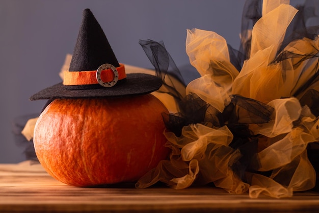 Halloween orange pumpkin in a witch hat on a blue background with black and orange tulle Copy space