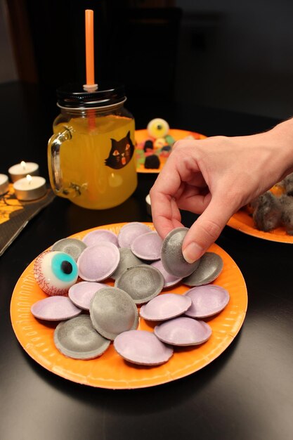 Halloween party Hand takes candy shaped like UFO on orange plate with sweets and jelly eyeball