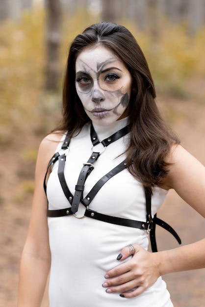 Halloween portrait of a young beautiful girl in a white dress with makeup on her face Posing in the autumn forest Skeleton face makeup The day of the Dead