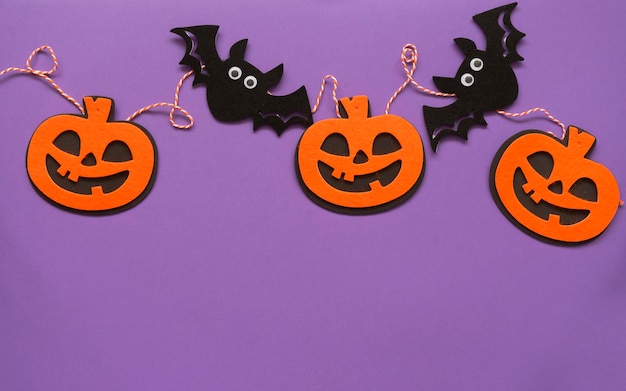 Halloween pumpkin and bat garland on purple background