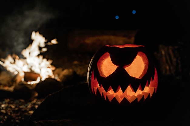 Halloween pumpkin face with candle lit and fire camp in the background Spooky face and pond fire