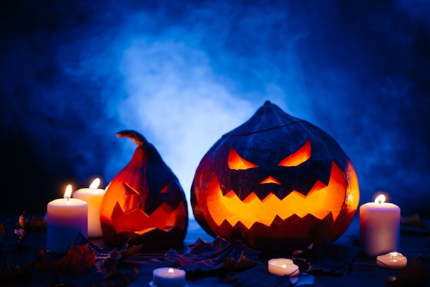 Halloween pumpkins with cut out horrible faces on a dark blue background with fog by candlelight.