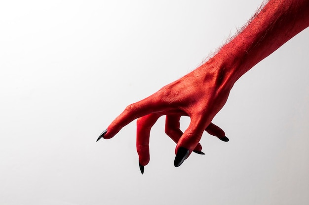 Halloween red devil monster hand with black fingernails against a plain background