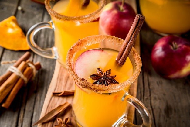 Halloween, Thanksgiving. Traditional autumn, winter drinks and cocktails. Spicy hot pumpkin sangria, with apple, cinnamon, anise. On old rustic wooden table, in glass mugs. Selective focus copy space