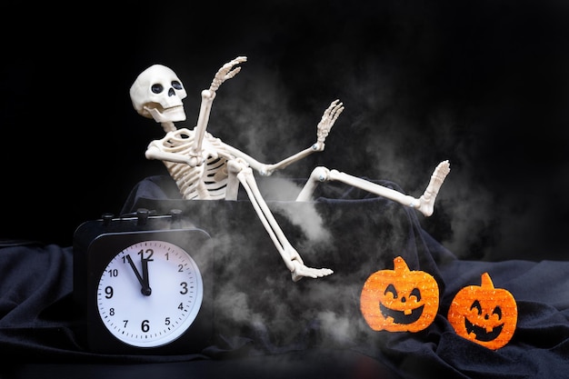 Halloween time A skeleton crawling out of a tomb a skull a clock on a black smoky dusty background