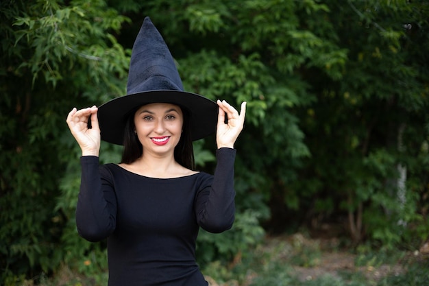 Halloween A young beautiful woman in a witch39s hat and a black dress in the park Space for text