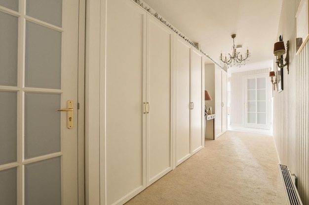 A hallway with white closet doors and chandels on either side of the room there is an open door that leads to another room