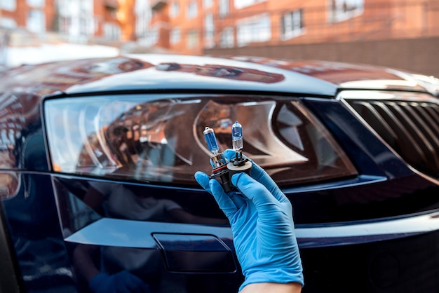 Halogen bulb in a man's hand against the background of the headlights of a beautiful car