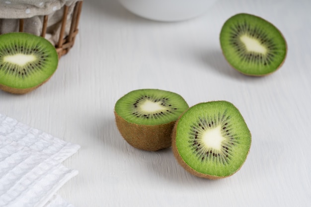 Halved ripe green kiwi fruit slices served on white wooden table with towel