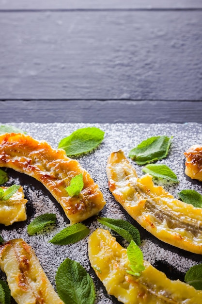 Halves of grilled bananas with powdered sugar on slate board Baked banana dessert with mint