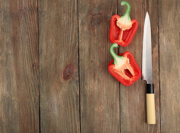 Halves of pepper with knife on wooden background