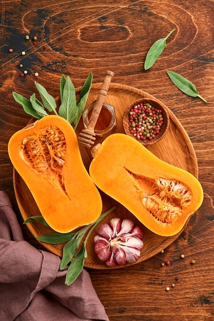 Halves of raw organic butternut squash with sage leaf, multicolored pepper garlic, honey, salt and pepper on old wooden background. Food background. Top view with copy space.