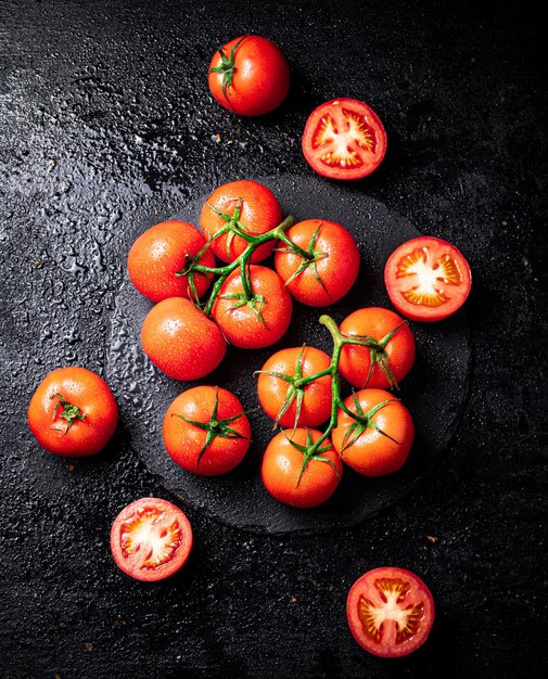 Halves and whole tomatoes on a branch on a stone board