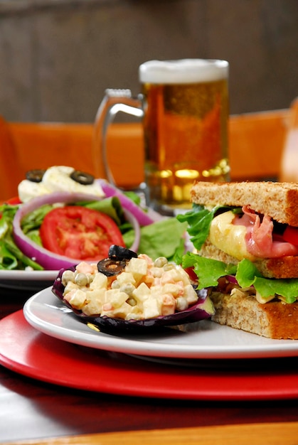 Ham and cheese gratin sandwich, Russian and green salad with cheese, jar of beer, food