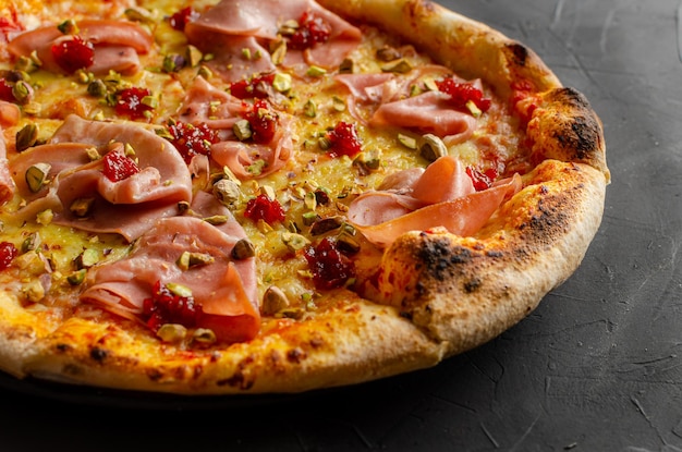 Ham pizza prepared in a wood-fired oven, black background. Closed up.