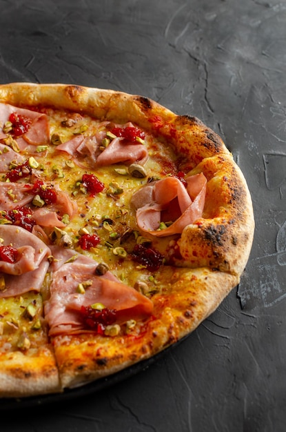 Ham pizza prepared in a wood-fired oven, black background.