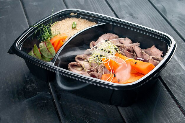 Ham with couscous and vegetables in containers on a black wooden background Takeaway Diet and healthy food