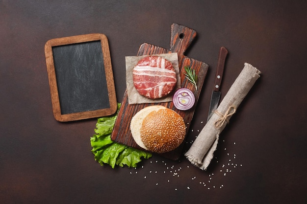 Hamburger ingredients raw cutlet lettuce bun cucumbers and onion on rusty background