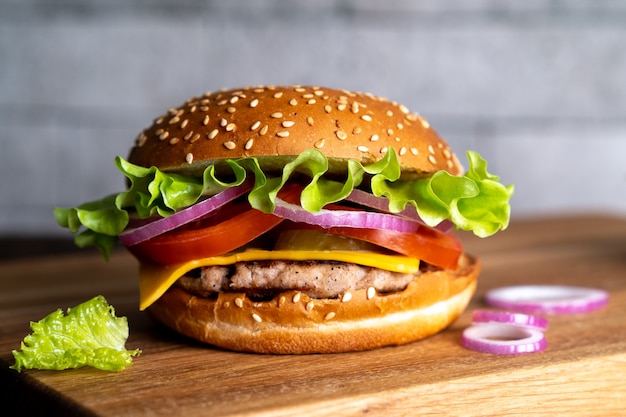 Hamburger with cutlet tomato cheese and lettuce leaves on a wooden board