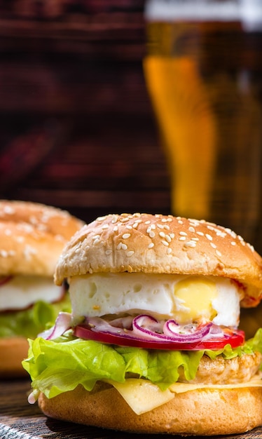 Hamburger with egg on a wooden board against the background of a glass with beer