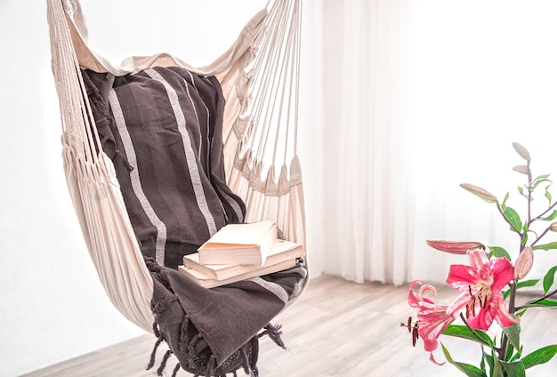 A hammock chair in boho style with a stack of books. The concept cozy place to relax at home.