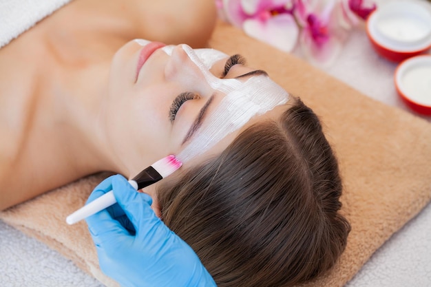 Hand applying nourishing mask on female face in spa salon