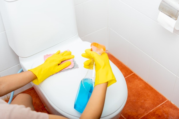 Hand of Asian woman cleaning toilet seat using liquid spray and pink cloth wipe restroom at house