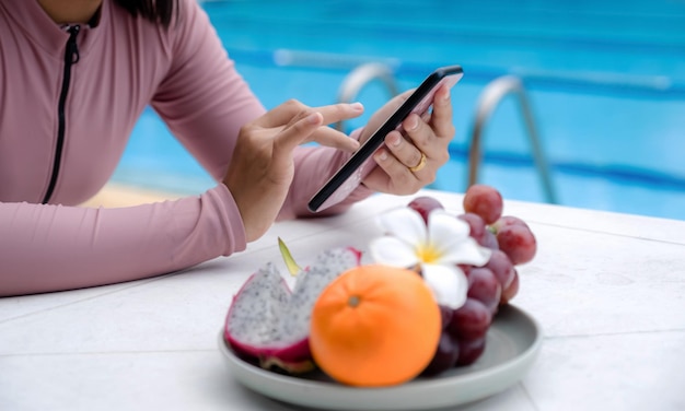 Hand of Asian woman in a swimsuit sitting by the hotel pool Sliding mobile phone for online shopping