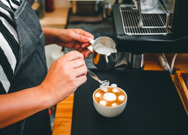 Hand of a barista in the coffee shop preparing to steam milk in the jug for a coffee cappuccino menu