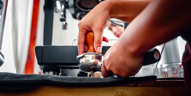 Hand of a barista holding a portafilter and a coffee tamper making an espresso coffee