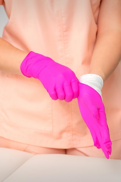 Hand of beautician puts on sterile pink gloves prepares to receive clients indoors.