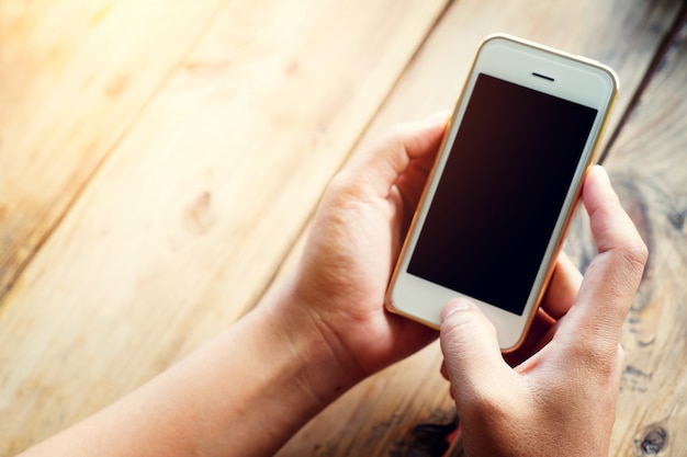 Photo hand of beautiful young hipster woman using smart phone in coffee shop, female watching her cell telephone while relaxing in cafe during free time.