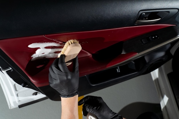 Hand in a black glove cleaning a car door coating with a soapy brush Detailing procedure Process of detailing the car door panel with detergent