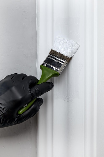 A hand in a black rubber glove paints a decorative door frame with white paint with a brush