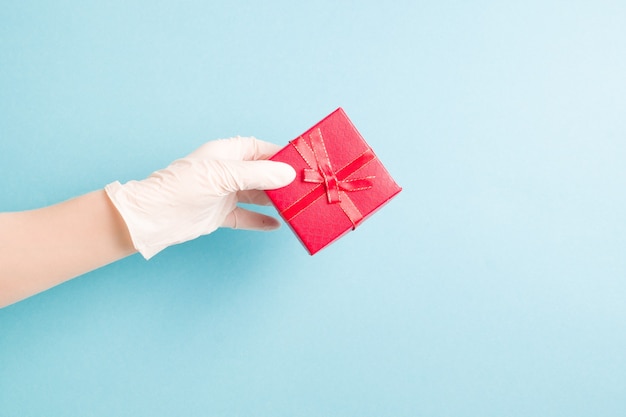 A hand in a blue disposable glove holds a red gift box light, blue background, copy space