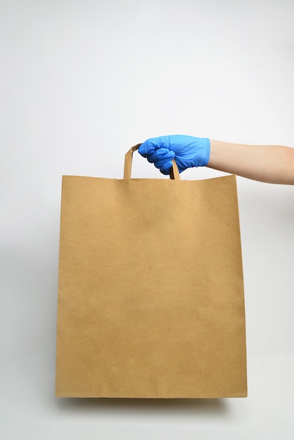 hand in blue medical gloves holds craft paper bag on white