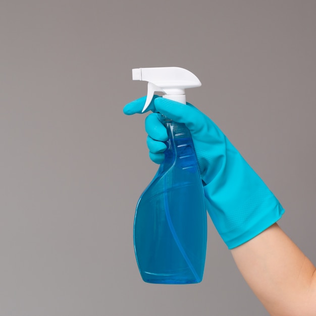 A hand in blue rubber glove holds the glass cleaner in a spray bottle 