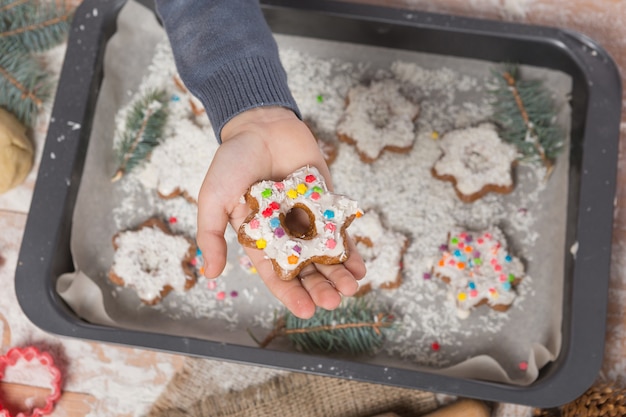 Hand of a boy holding a Christmas cookie over a baking tray