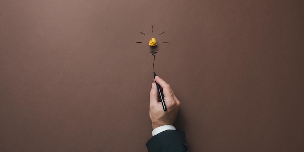 Hand of a businessman drawing a light bulb made of yellow wrinkled paper