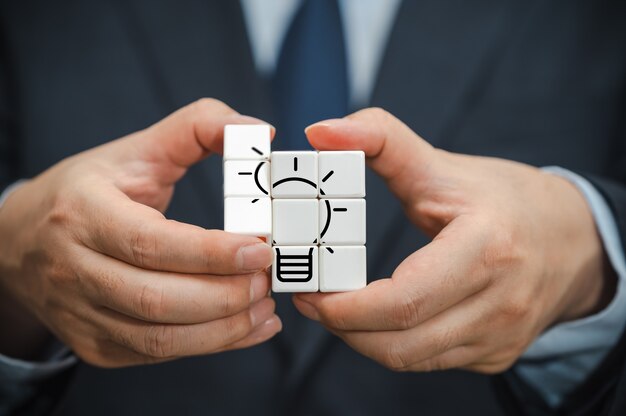 The hand of a businessman holding a cube with a view of the bulb Icon.