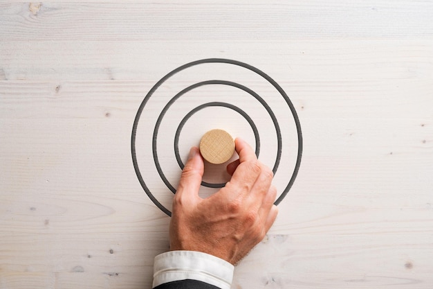 Hand of a businessman placing blank wooden cut circle in the middle of a target