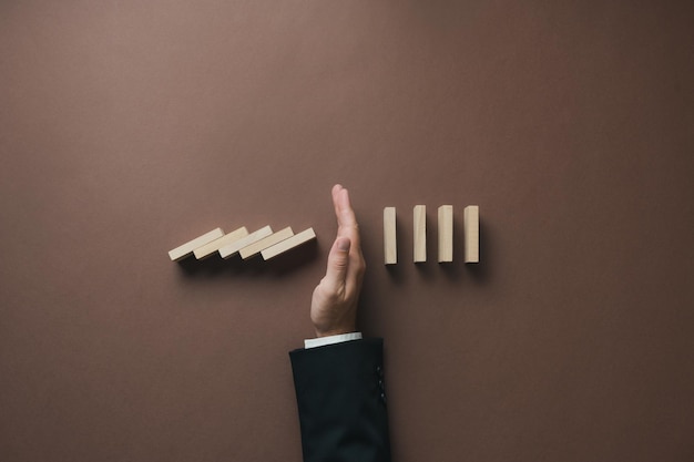 Hand of a businessman stopping falling dominos