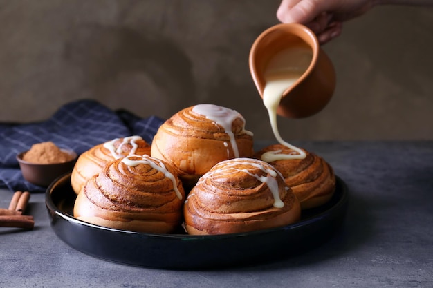 Hand of chef pouring fresh delicious cinnamon rolls with condensed milk