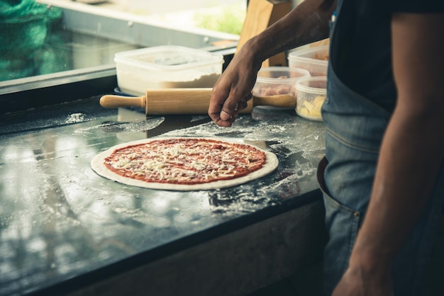 Hand Chef preparing spread cheese on pizza on marble table closeup making pizza