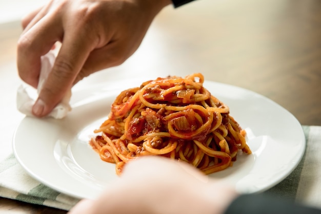 Hand of chef wiping dish of spaghetti bolognese 