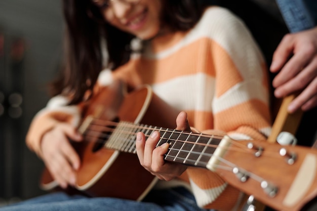 Hand of child learning to play guitar while keeping finger on one of strings